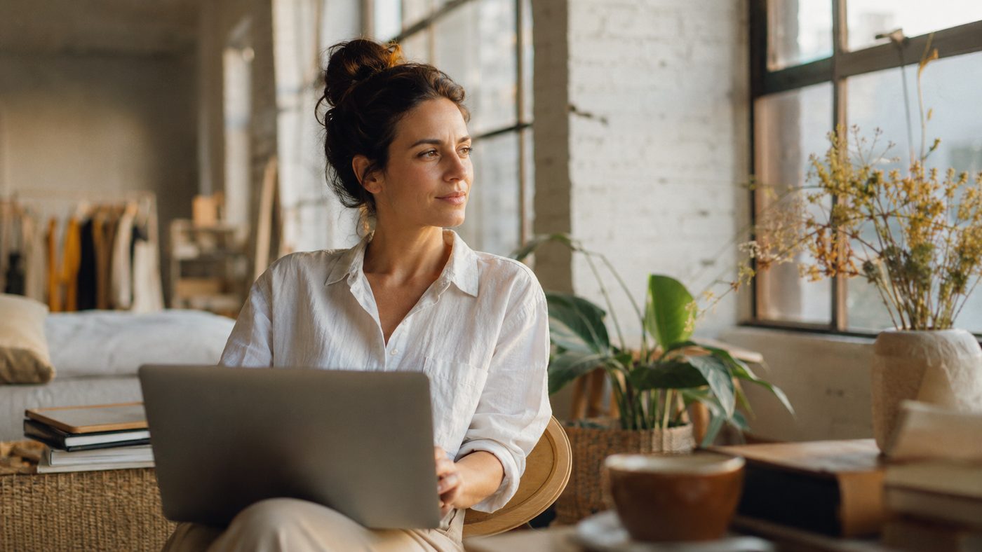 A creator working on a laptop in a sunlit loft, looking out the window